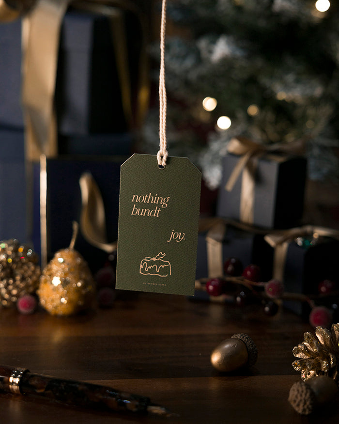 My Brunch Plans' gift tag with 'nothing bundt joy' text on a festive background with lights and ornaments.