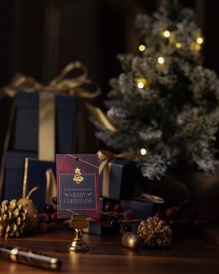 My Brunch Plans' Tartan linen gift tag with a dill pickle shaped into tree on a wooden surface with Christmas tree and presents.