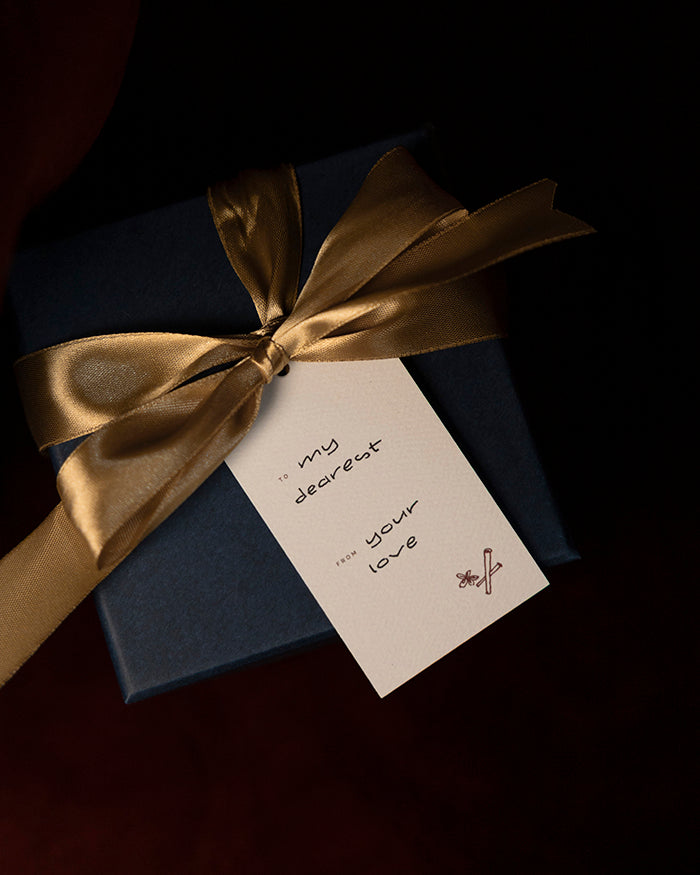 Navy blue gift box with gold ribbon and a My Brunch Plans' gift tag on a dark background. To: "my dearest" from "your love"