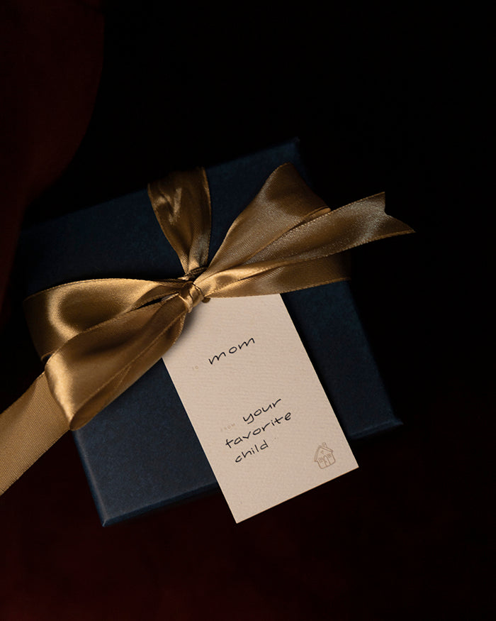Navy blue gift box with gold ribbon and a My Brunch Plans' gift tag on a dark background. To "mom" from "your favorite child"