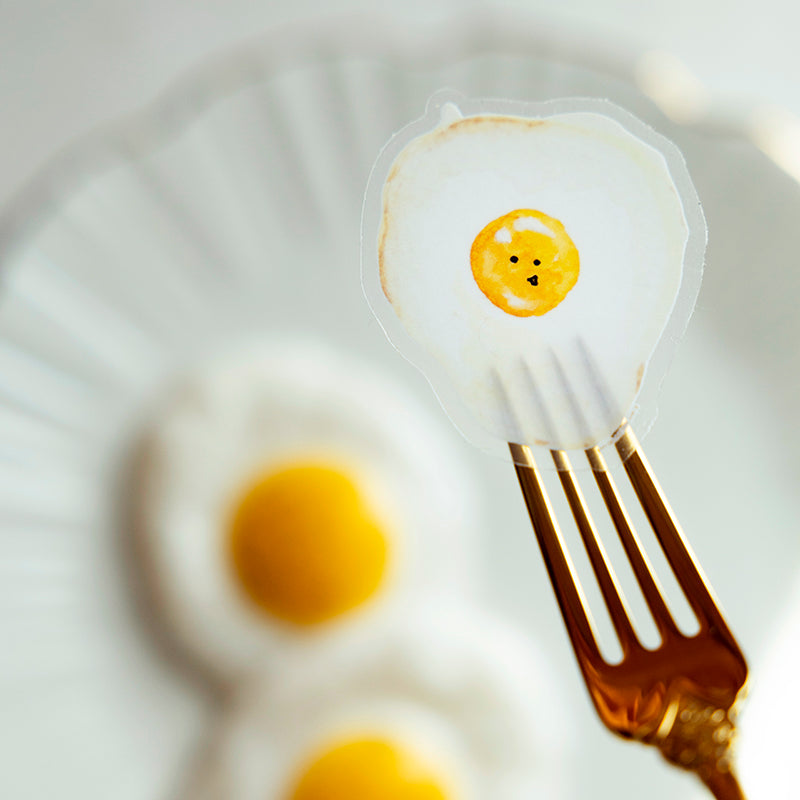 My Brunch Plans’ hand painted gouache Sunny Side Up Egg with smiley face diecut sticker on a fork with sunny side up eggs in the background.