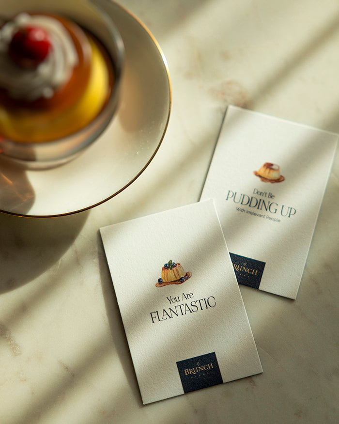 Flatlay of My Brunch Plans’ hand painted in gouache flan illustrations affirmational cards on a marble surface with a flan dessert in the background. "you are flantastic" " don't be pudding up with irrelavent people."