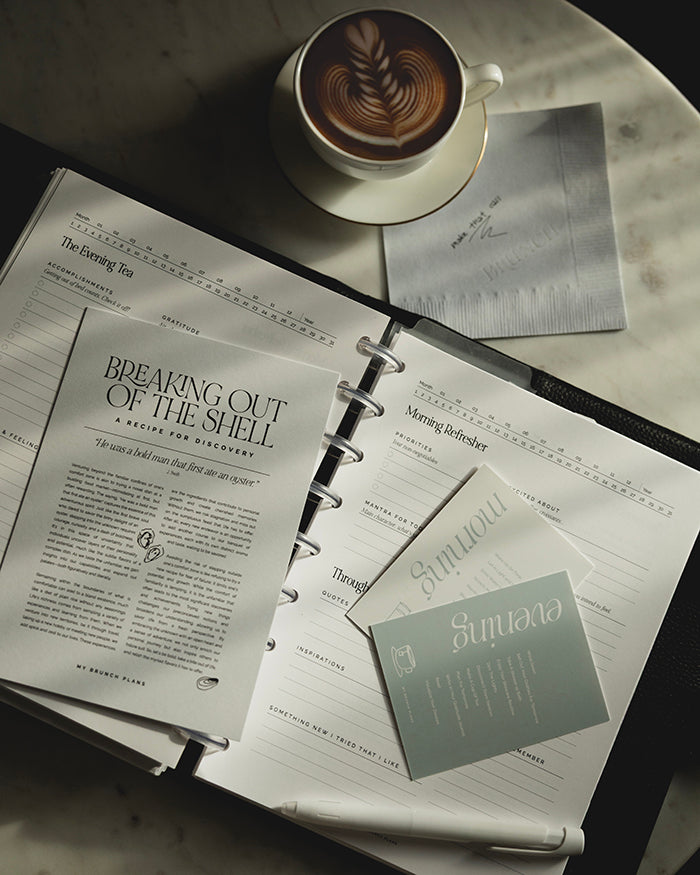 My Brunch Plans' planner card set of two. One is a morning routine suggestion with a hand drawn line art of lemon water with a white background and blue text. The evening routine card has hand drawn line art of a cup of tea with the same blue but as the background. Set of planner cards are placed on a discbound planner with a pen, latte, our napkin notepad, breaking out of the shell art print, and morning refresher insert.