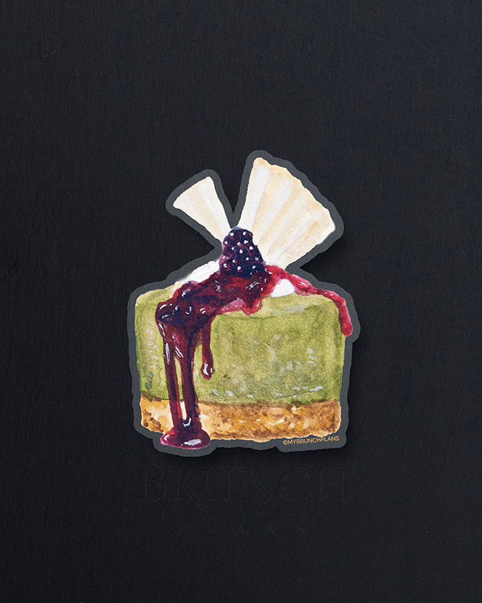 My Brunch Plans' hand painted gouache matcha cheesecake with blackberry compote and white chocolate topper diecut vinyl sticker with the paper backing on a marble background.