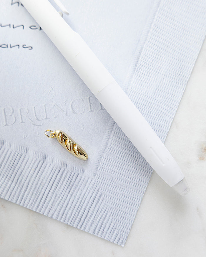 Baguette Charm | 18k Gold Plated on My Brunch Plans’ Napkin notepad with a pen for size comparison.