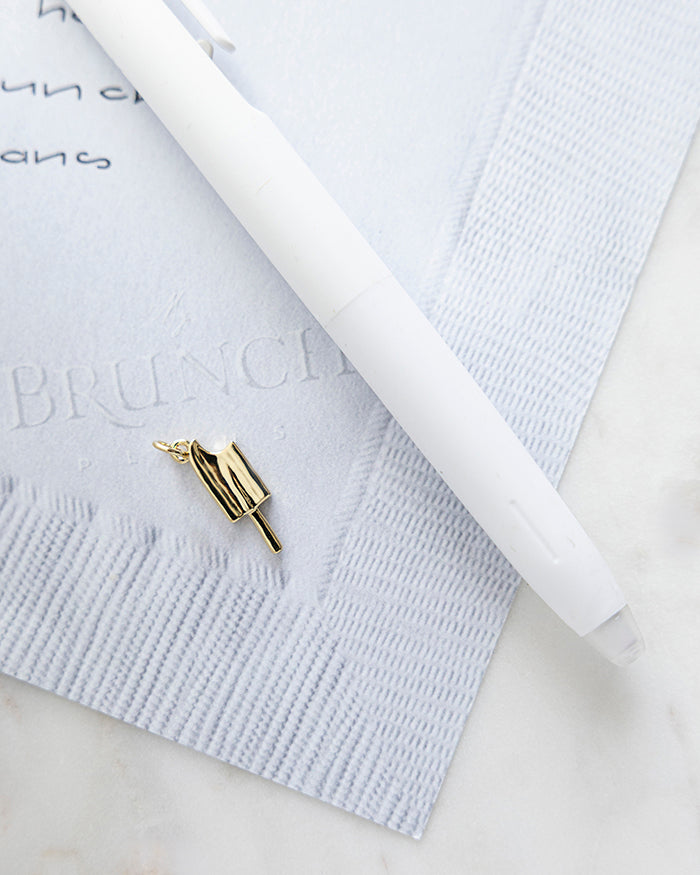 Popsicle Charm | 18k Gold Plated on My Brunch Plans’ Napkin notepad with a pen for size comparison.