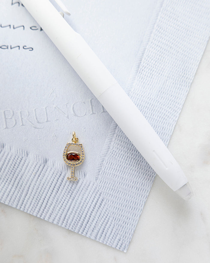 Red Wine Charm | 18k Gold Plated with CZ on My Brunch Plans’ Napkin notepad with a pen for size comparison.