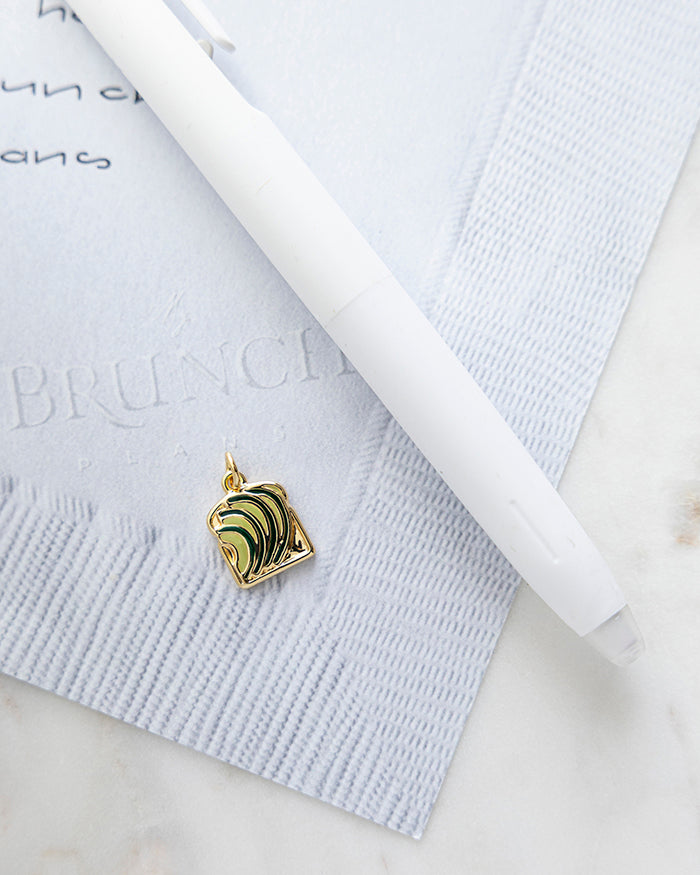 Avocado Toast Charm | 18k Gold Plated with Enamel on My Brunch Plans’ Napkin notepad with a pen for size comparison.