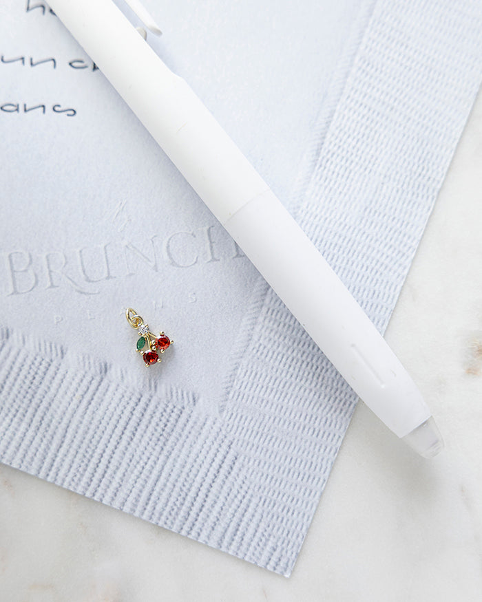 Cherry Charm | 18k Gold Plated with CZ on My Brunch Plans’ Napkin notepad with a pen for size comparison.