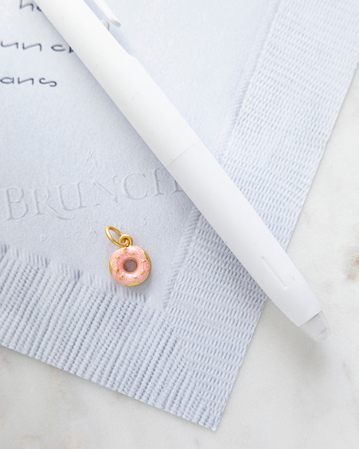 Pink Donut Charm | 24k Gold Plated with Enamel on My Brunch Plans’ Napkin notepad with a pen for size comparison.