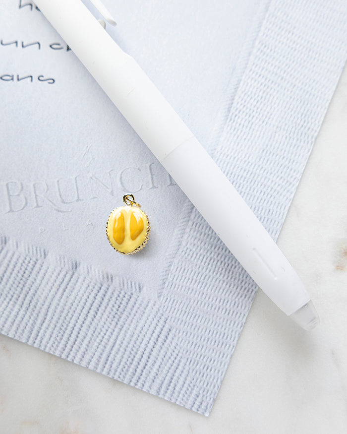 Durian Charm | 18k Gold Plated with Enamel on My Brunch Plans’ Napkin notepad with a pen for size comparison.
