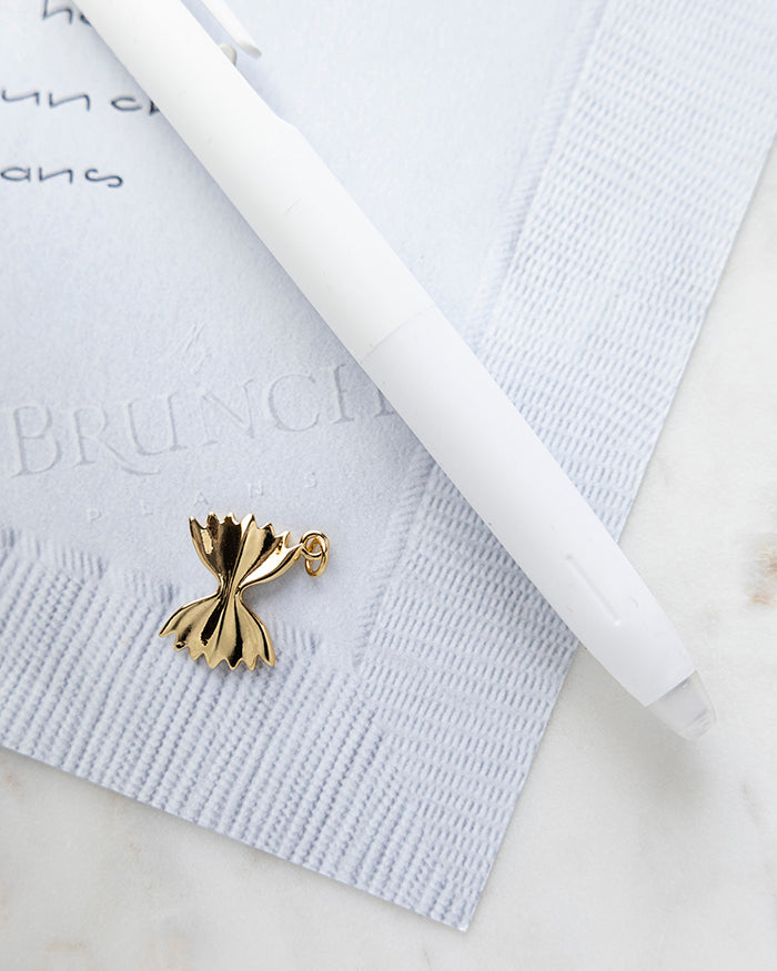 Farfelle Charm | 18k Gold Plated on My Brunch Plans’ Napkin notepad with a pen for size comparison.