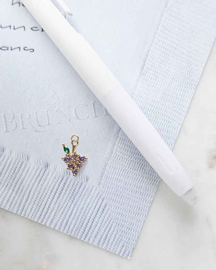 Grape Charm | 18k Gold Plated with CZ on My Brunch Plans’ Napkin notepad with a pen for size comparison.