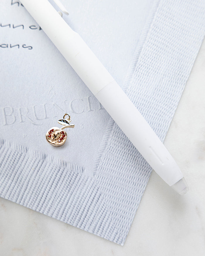 Nectarine Charm | 18k Gold Plated with CZ on My Brunch Plans’ Napkin notepad with a pen for size comparison.