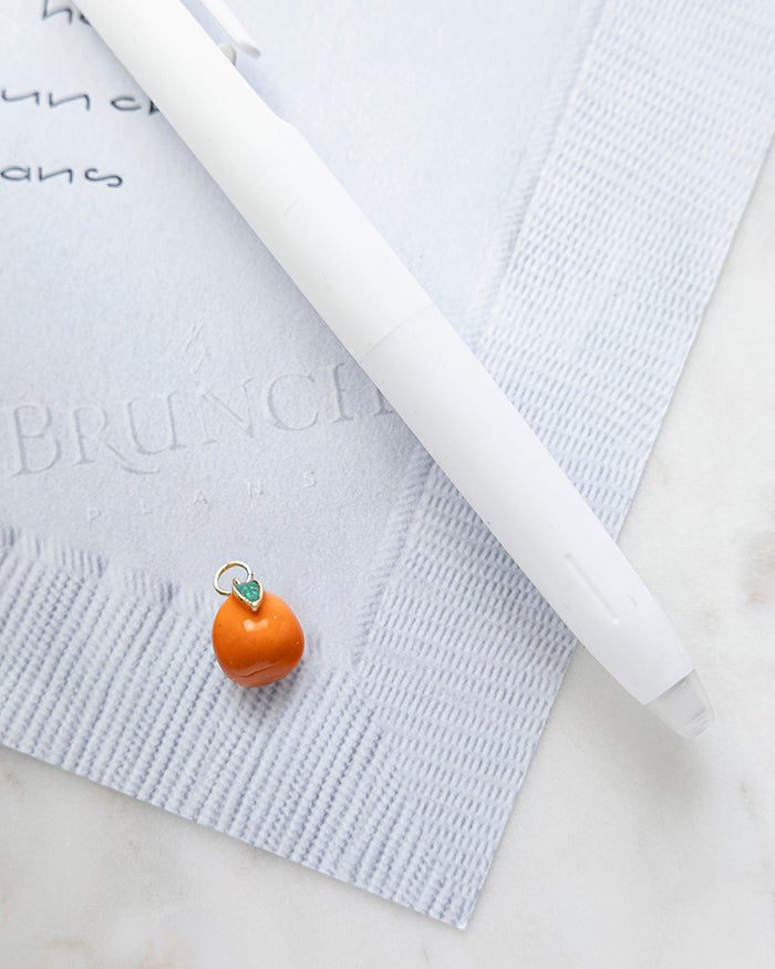 Orange Charm | 18k Gold Plated with Enamel on My Brunch Plans’ Napkin notepad with a pen for size comparison.