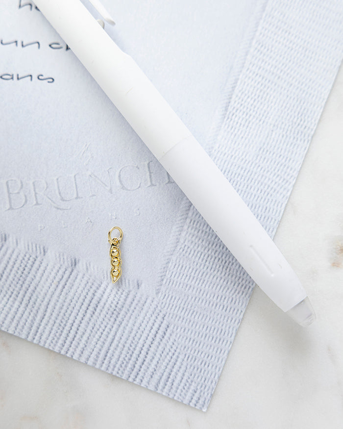 Peas in a Pod Charm | 18k Gold Plated on My Brunch Plans’ Napkin notepad with a pen for size comparison.
