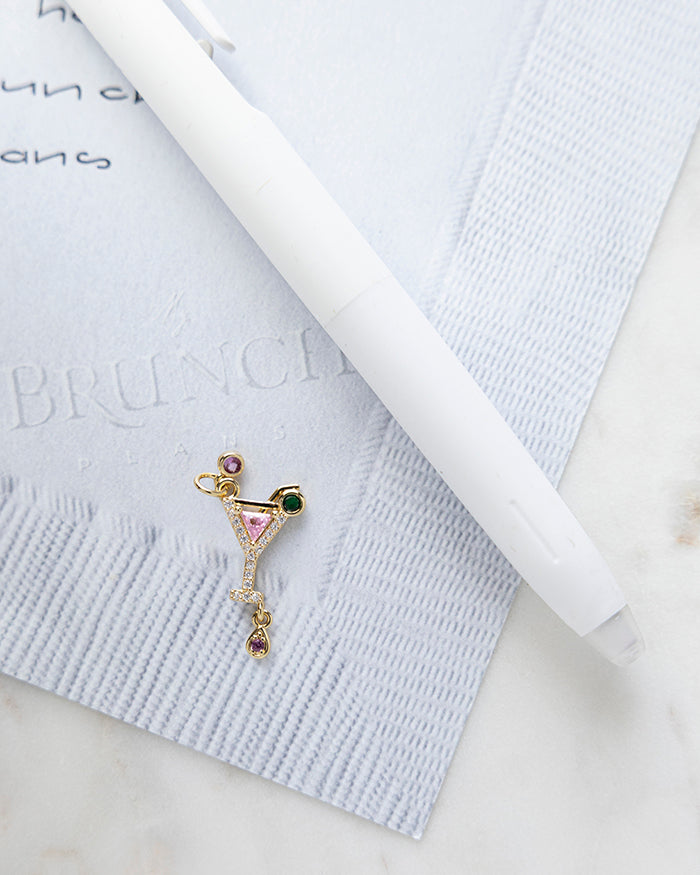 Pink Martini Charm | 18k Gold Plated with CZ on My Brunch Plans’ Napkin notepad with a pen for size comparison.