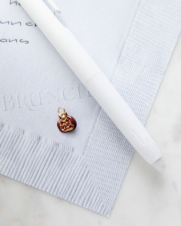 Red Pomegranate Charm | 18k Gold Plated with CZ on My Brunch Plans’ Napkin notepad with a pen for size comparison.