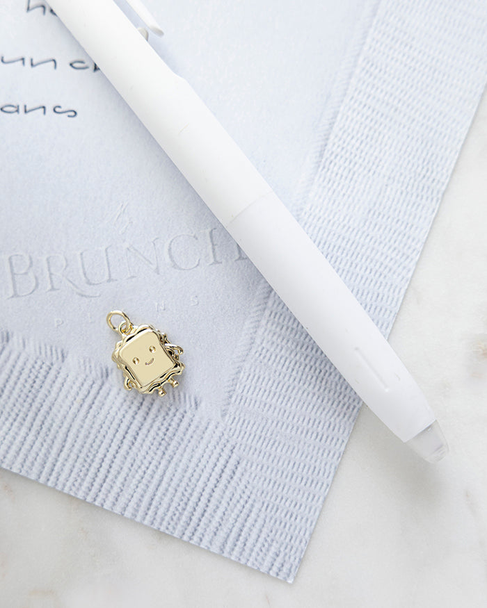 Smily Sandwich Charm | 18k Gold Plated with Enamel on My Brunch Plans’ Napkin notepad with a pen for size comparison.
