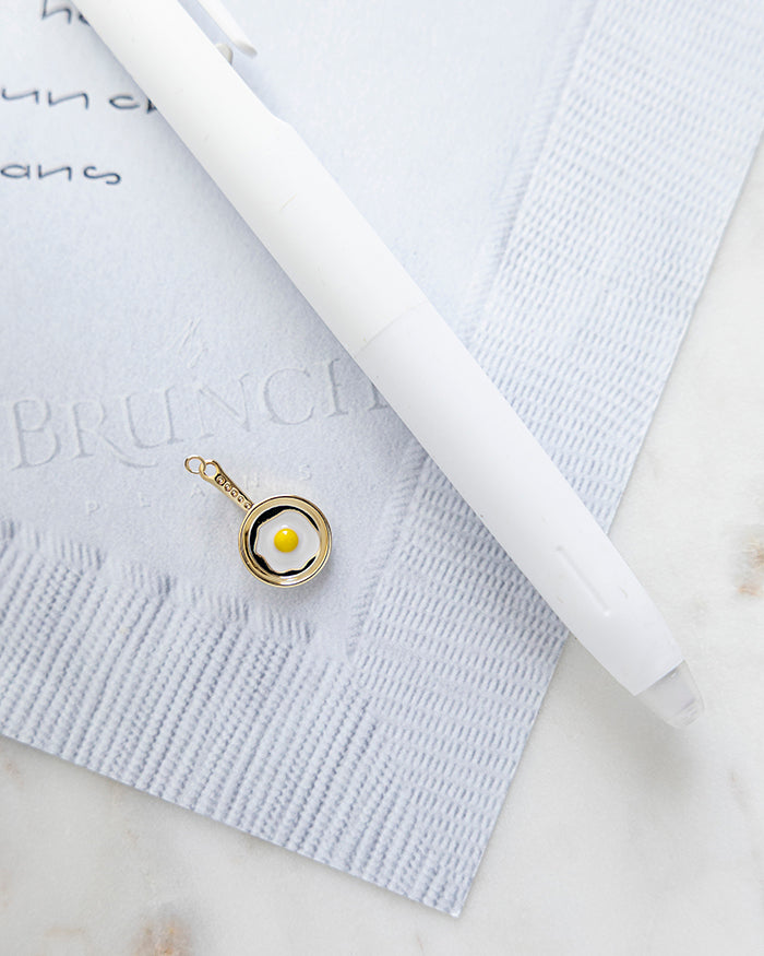 Egg Skillet Charm | 18k Gold Plated with Enamel on My Brunch Plans’ Napkin notepad with a pen for size comparison.